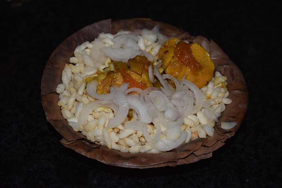 Puffed rice, onion and a chicken curry serving in a leaf bowl.