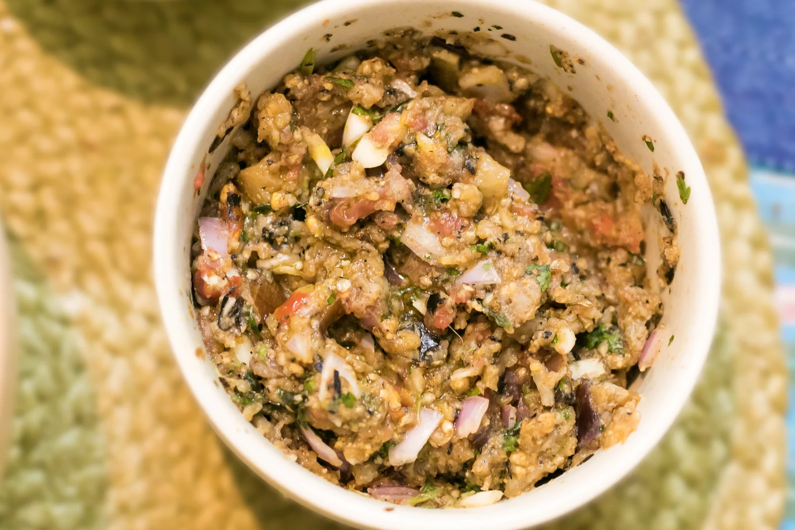 A bowl of combined roasted eggplant and tomato mash with onion and herbs.