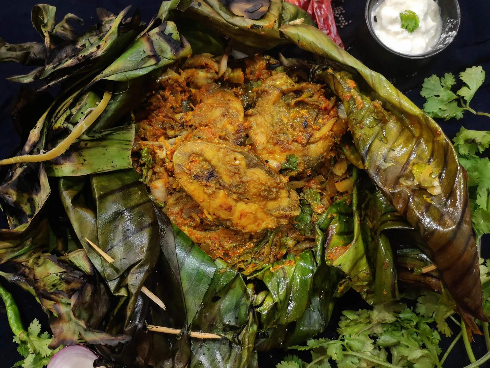 Fish steaks in an opened, charred leaf parcel with a yellow spice coating.