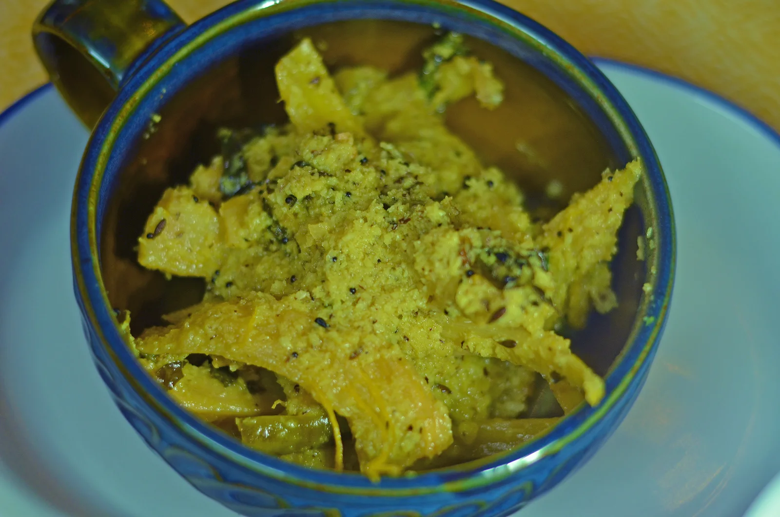 Cooked elephant-apple pieces with coconut and seeds in a blue-rimmed bowl.
