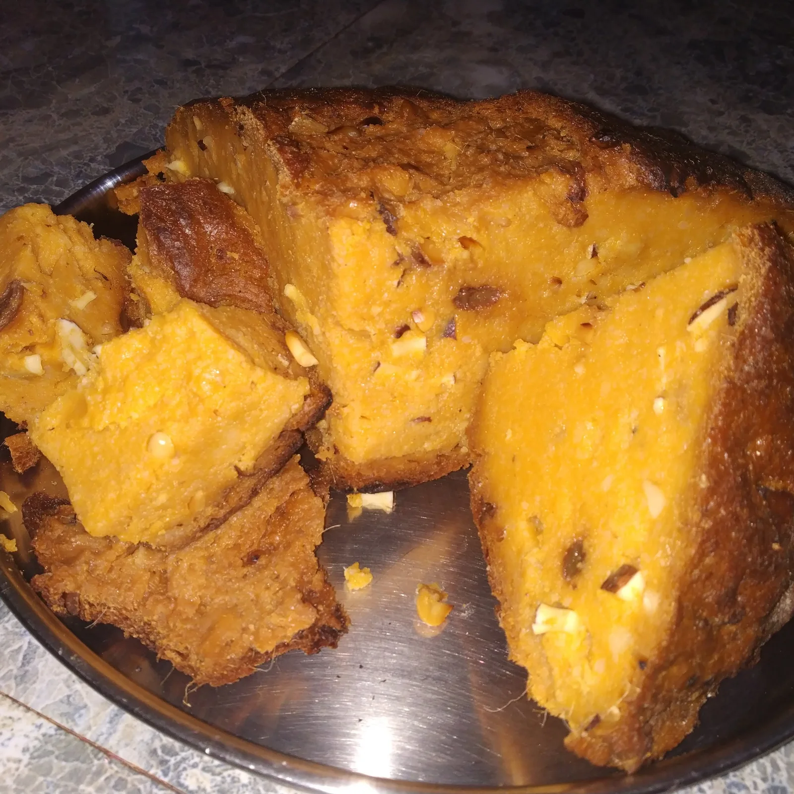 Slices of golden tala poda pitha with a browned crust on a metal plate.