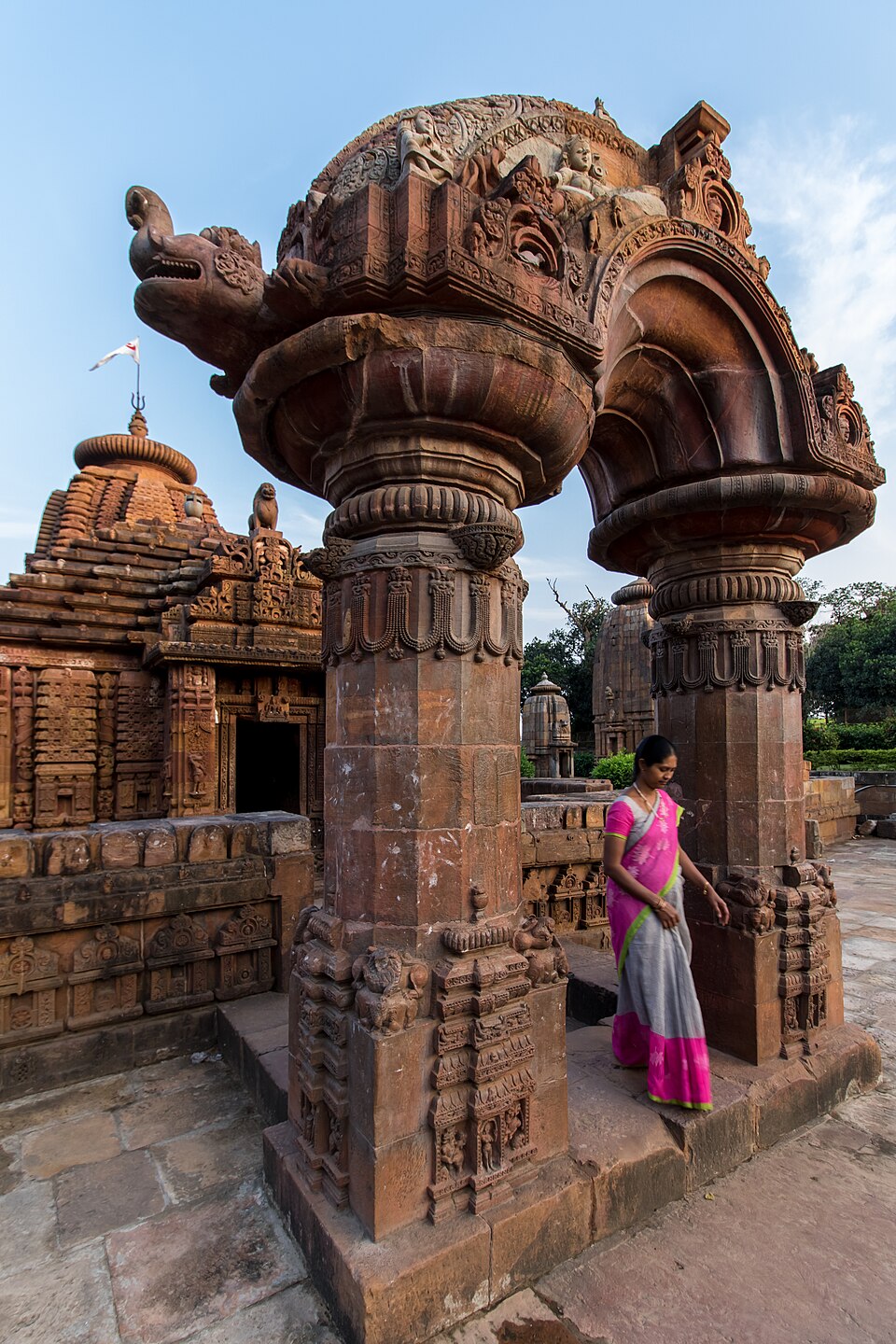 A carved stone arch at Mukteswar, with the temple behind it and a visitor passing beneath.