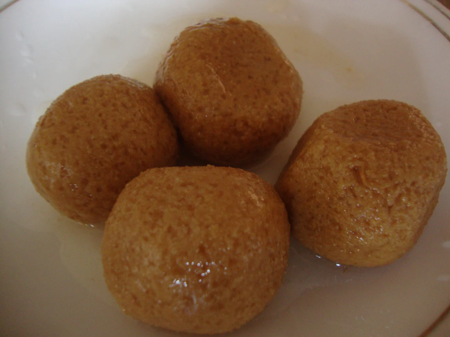 Four brown rasagola sweets in syrup on a pale plate.
