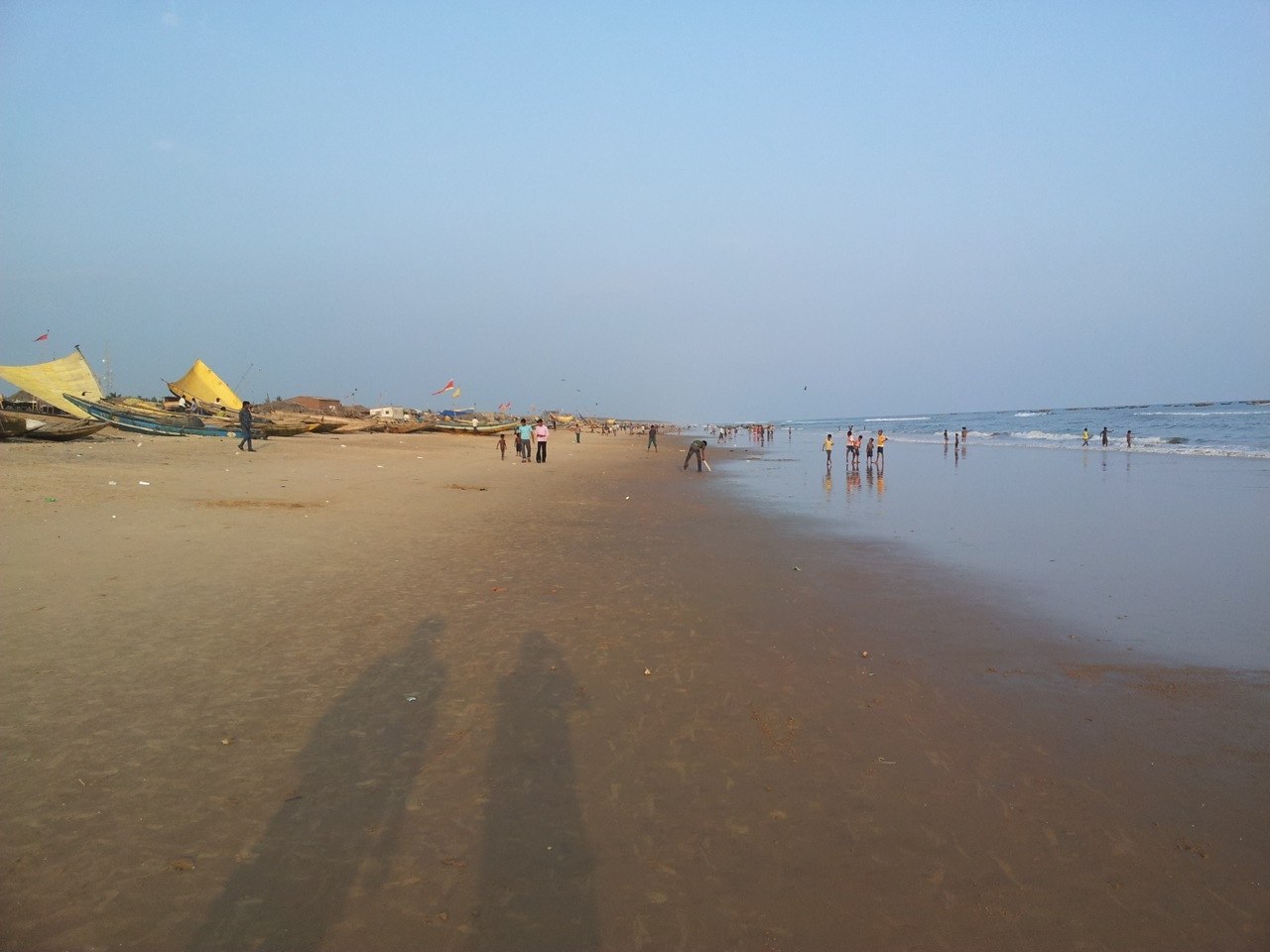 People walking on wet sand beside the sea at Puri beach.