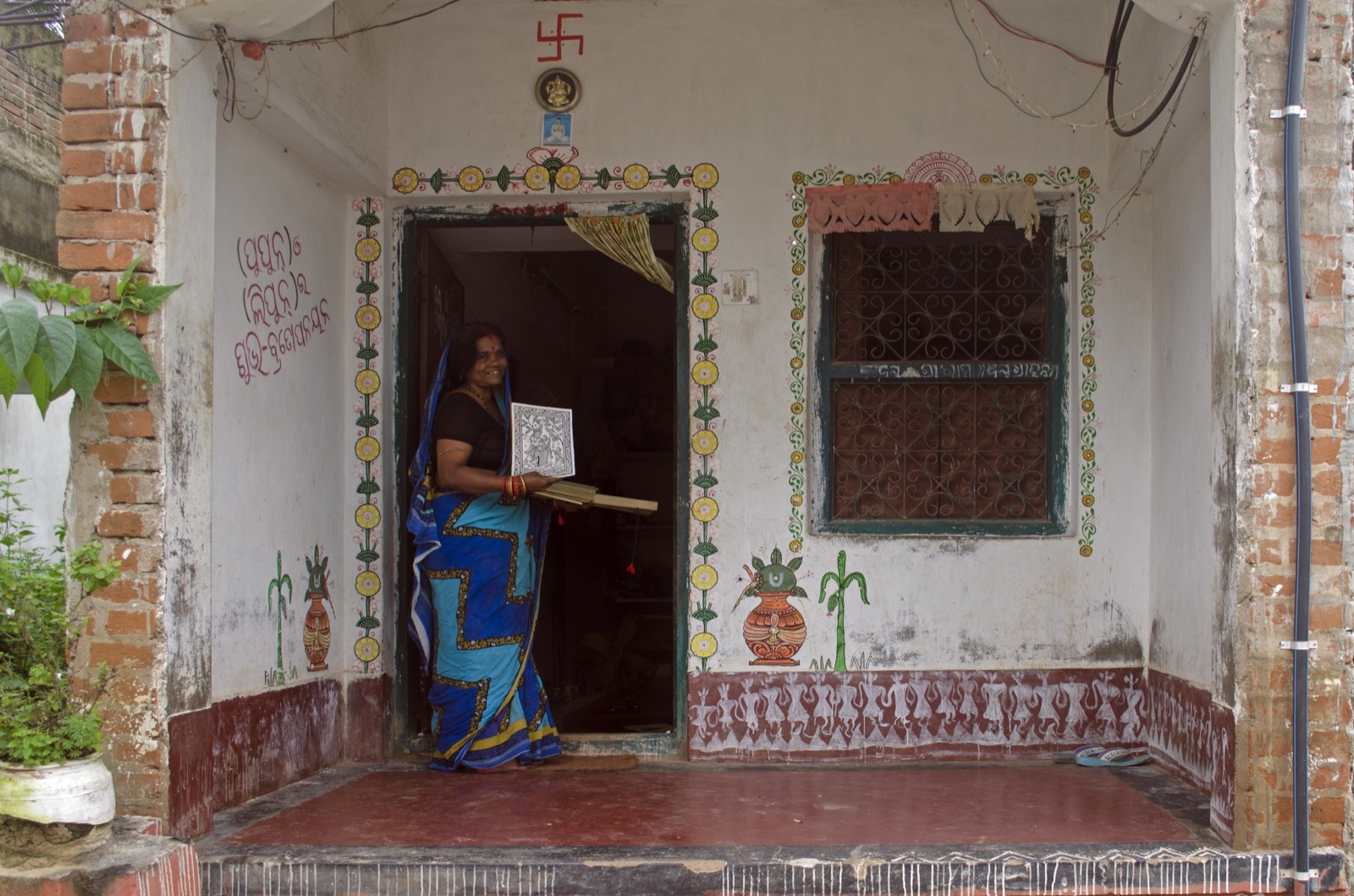 An artisan holding a work of art in the doorway of a painted house in Raghurajpur.