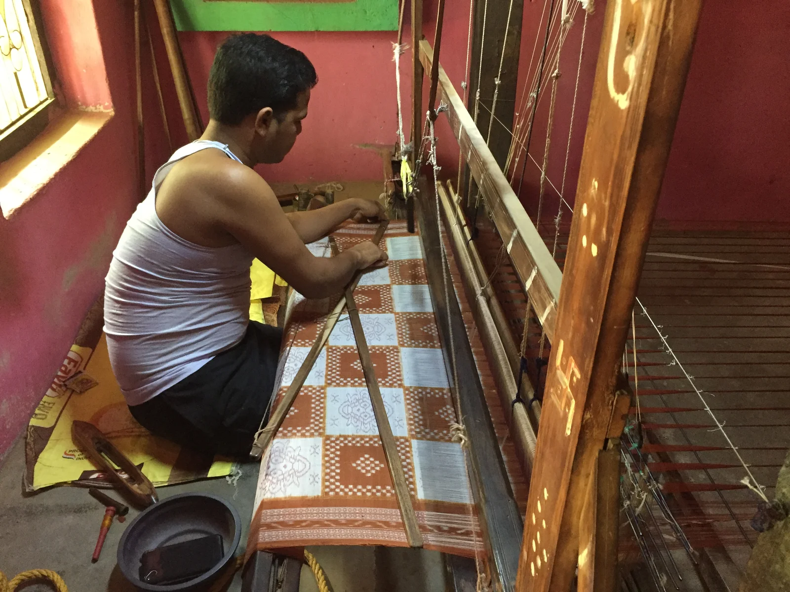 A weaver seated at a loom with patterned cloth stretched in front of him
