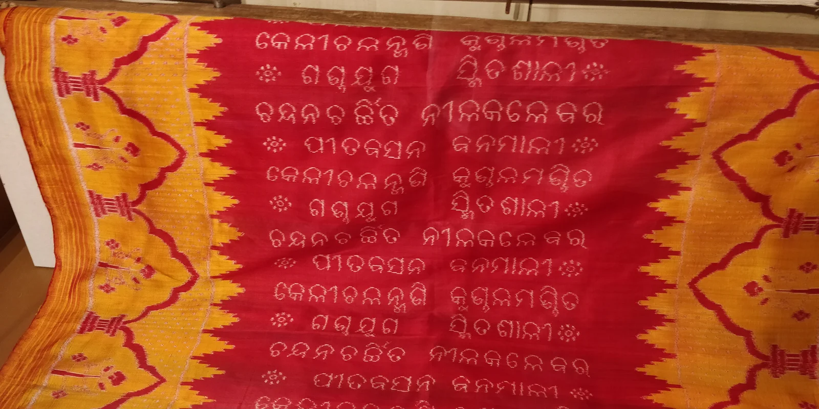 Red and yellow Khandua textile bearing rows of woven Odia lettering